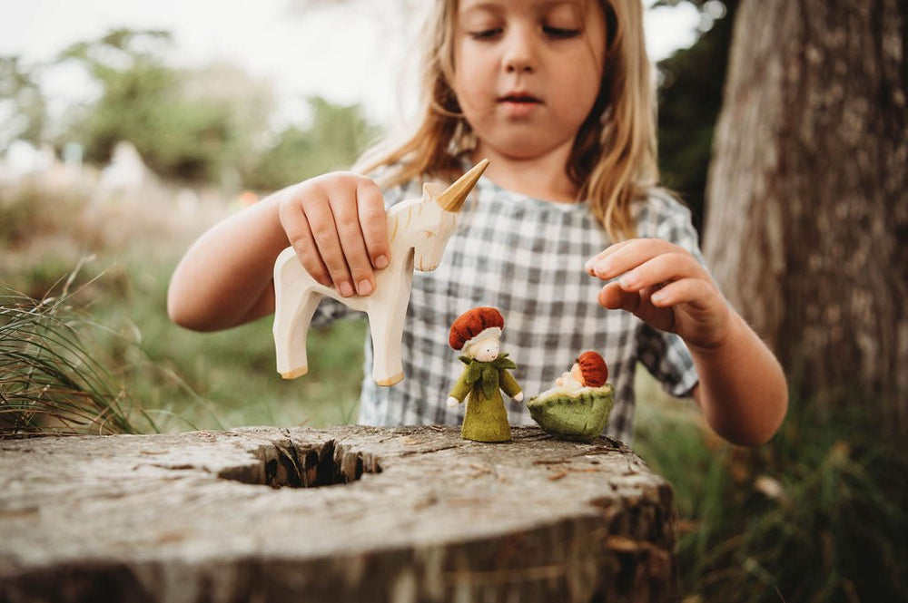 girl playing with Ostheimer unicorn and felt dolls in the forest